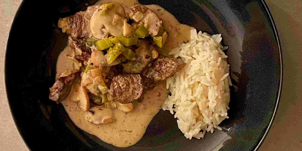 Damwild Stroganoff mit Beilage auf dunklem Teller